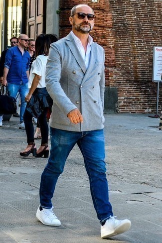 Come indossare e abbinare un blazer doppiopetto grigio per un uomo di 50 anni: Indossa un blazer doppiopetto grigio con jeans blu per creare un look smart casual. Perché non aggiungere un paio di sneakers basse in pelle bianche per un tocco più rilassato?