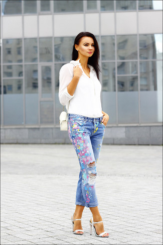 Look alla moda per donna: Blusa abbottonata bianca, Jeans stampati blu, Sandali con tacco in pelle argento, Borsa a tracolla in pelle bianca