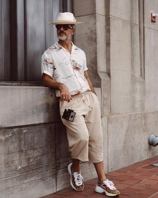 Moda uomo anni 50: Per un outfit quotidiano pieno di carattere e personalità, indossa una camicia a maniche corte stampata bianca con pantaloncini di lino beige. Opta per un paio di scarpe sportive multicolori per avere un aspetto più rilassato.