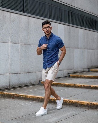 Look alla moda per uomo: Camicia a maniche corte in chambray blu, Pantaloncini beige, Sneakers basse di tela bianche, Occhiali da sole trasparenti