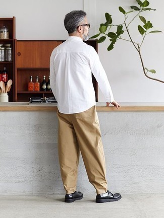 Moda uomo anni 50: Mostra il tuo stile in una camicia a maniche lunghe bianca con chino marrone chiaro per un pranzo domenicale con gli amici. Completa il tuo abbigliamento con un paio di scarpe double monk in pelle nere.