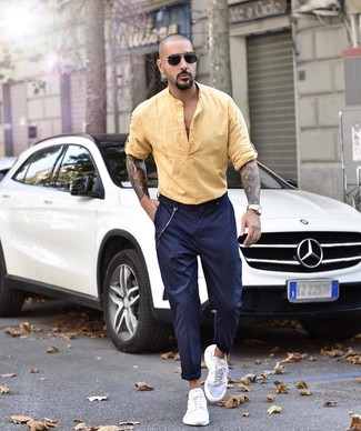 Look alla moda per uomo: Camicia a maniche lunghe di lino gialla, Chino a righe verticali blu scuro, Scarpe sportive bianche, Occhiali da sole neri
