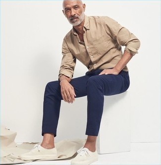 Moda uomo anni 50 quando fa caldo: Scegli un outfit composto da una camicia a maniche lunghe marrone chiaro e chino blu scuro per vestirti casual. Per distinguerti dagli altri, mettiti un paio di sneakers basse di tela bianche.