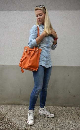 Look alla moda per donna: Camicia di jeans azzurra, Jeans aderenti blu, Sneakers alte di tela bianche, Borsa shopping in pelle arancione