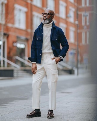 Moda uomo anni 50 in primavera 2025: Questa combinazione di una camicia giacca blu scuro e pantaloni cargo bianchi è perfetta per il tempo libero. Sfodera il gusto per le calzature di lusso e scegli un paio di mocassini con nappine in pelle marrone scuro come calzature. Ecco un look ideale per questa primavera.