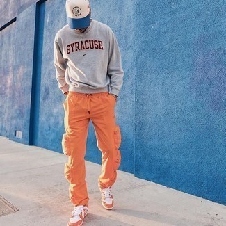 Look alla moda per uomo: Felpa stampata grigia, Pantaloni cargo arancioni, Sneakers basse in pelle arancioni, Berretto da baseball bianco e blu scuro
