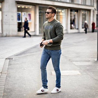 Look alla moda per uomo: Felpa stampata verde oliva, Jeans aderenti blu, Sneakers basse in pelle stampate bianche