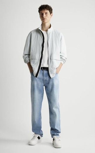 Look alla moda per uomo: Giacca a vento grigia, T-shirt girocollo bianca, Jeans azzurri, Sneakers basse in pelle bianche e nere