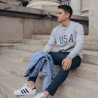 Look alla moda per uomo: Giacca di jeans azzurra, Felpa stampata grigia, Chino blu scuro, Sneakers basse in pelle bianche e nere