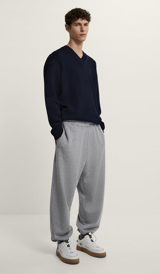 Look alla moda per uomo: Maglione con scollo a v blu scuro, Pantaloni sportivi grigi, Sneakers basse in pelle bianche, Calzini grigio scuro