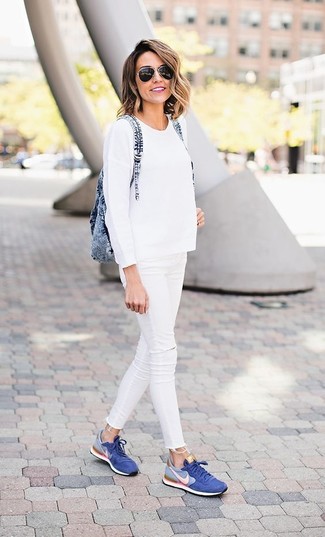 Look alla moda per donna: Maglione girocollo bianco, Jeans aderenti strappati bianchi, Sneakers basse blu, Zaino di jeans blu
