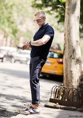 Moda uomo anni 50 in modo rilassato: Un polo blu scuro e chino blu scuro si adattano perfettamente a ogni genere di attività per il weekend. Per un look più rilassato, indossa un paio di sandali in pelle scamosciata blu scuro.