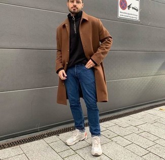 Trend da uomo 2024 quando fa gelo: Indossa un soprabito marrone e jeans blu scuro, perfetto per il lavoro. Calza un paio di scarpe sportive beige per avere un aspetto più rilassato.