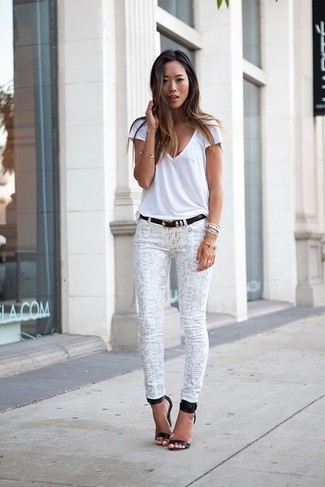 Come indossare e abbinare jeans bianchi in modo smart-casual: Metti una t-shirt con scollo a v bianca e jeans bianchi per un semplice tocco di eleganza. Questo outfit si abbina perfettamente a un paio di sandali con tacco in pelle neri.