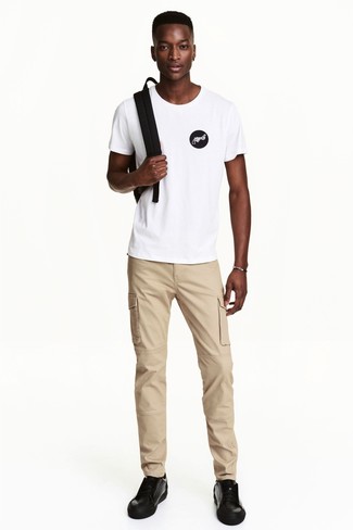 Look alla moda per uomo: T-shirt girocollo stampata bianca e nera, Chino marrone chiaro, Sneakers basse in pelle nere, Zaino nero