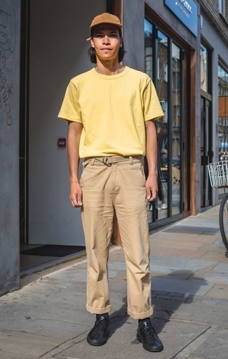 Look alla moda per uomo: T-shirt girocollo gialla, Chino marrone chiaro, Sneakers basse in pelle nere, Berretto da baseball marrone chiaro