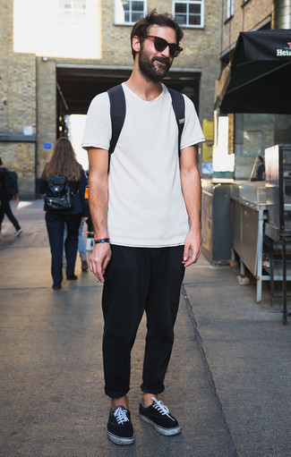 Look alla moda per uomo: T-shirt girocollo bianca, Chino neri, Sneakers basse in pelle scamosciata nere e bianche, Zaino di tela blu scuro