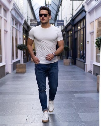 Come indossare e abbinare jeans blu scuro quando fa molto caldo: Coniuga una t-shirt girocollo bianca con jeans blu scuro per affrontare con facilità la tua giornata. Un paio di sneakers basse di tela bianche si abbina alla perfezione a una grande varietà di outfit.